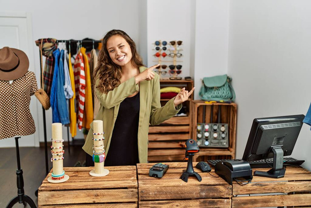 Piękna Latynoska kobieta pracująca w sklepie z modą uśmiechnięta i patrząca w kamerę z dwoma rękami i palcami na boku.  - Zdjęcie, obraz