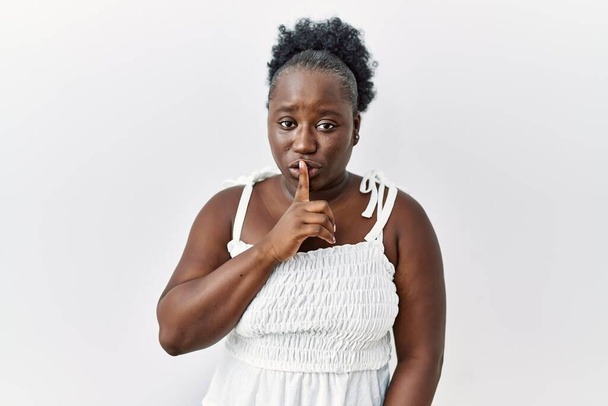 Young african woman standing over white isolated background asking to be quiet with finger on lips. silence and secret concept.  - Foto, Bild