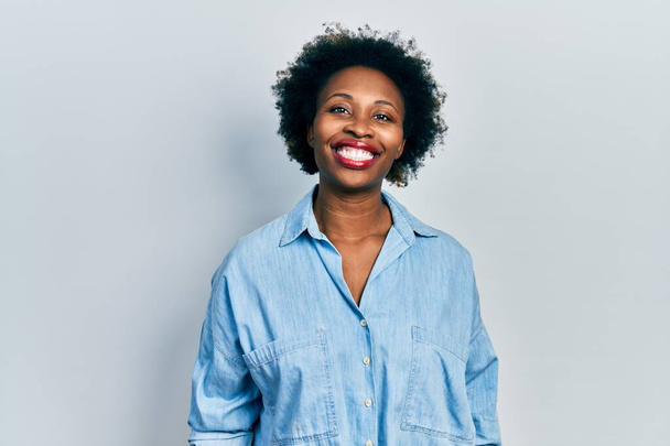 Joven mujer afroamericana vistiendo ropa casual con aspecto positivo y feliz de pie y sonriendo con una sonrisa confiada mostrando los dientes  - Foto, imagen