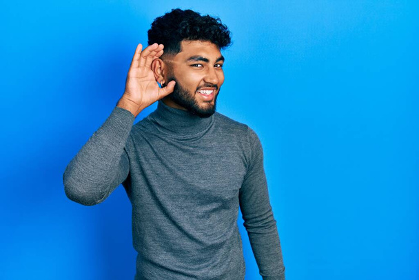 Uomo arabo con la barba che indossa maglione dolcevita sorridente con mano sull'orecchio ascoltando voci o pettegolezzi. concetto di sordità.  - Foto, immagini