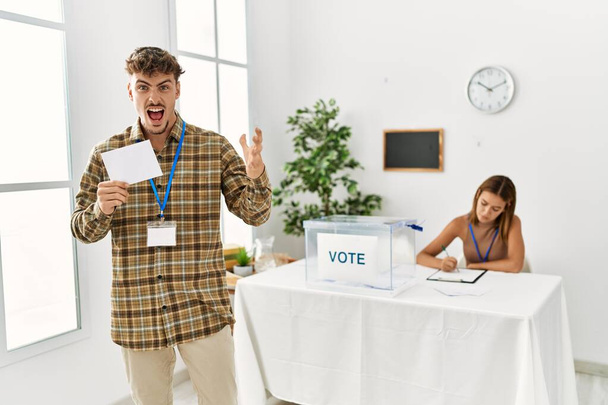 Молодий красивий чоловік голосує, кладе конверт у виборчу скриньку, святкуючи перемогу з щасливою посмішкою і виразом переможця з піднятими руками
  - Фото, зображення