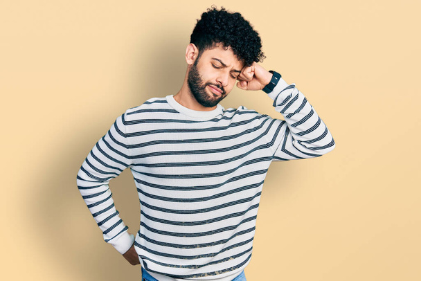 Junger arabischer Mann mit Bart trägt lässig gestreiften Pullover, der sich nach hinten streckt, müde und entspannt, schläfrig und gähnt für den frühen Morgen  - Foto, Bild