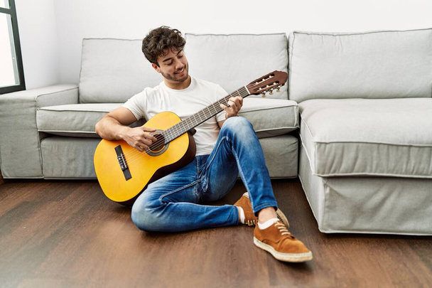Jovem hispânico sorrindo confiante tocando guitarra clássica em casa - Foto, Imagem