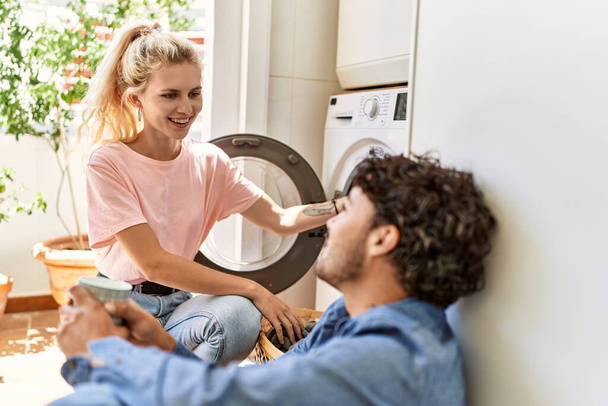 Young couple smiling happy drinking coffee while doing laundry at home. - Foto, Bild