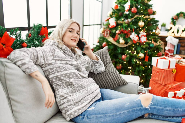 Молода біла дівчина сидить на дивані, розмовляючи на смартфоні вдома
. - Фото, зображення