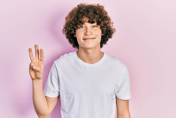 Handsome young man wearing casual white t shirt showing and pointing up with fingers number three while smiling confident and happy.  - Photo, Image