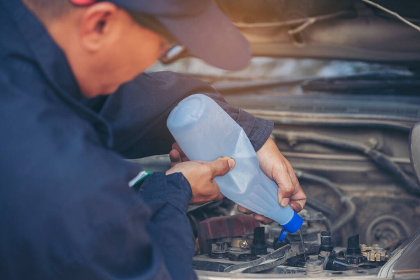 Car Mechanic man hands pouring Deionized purified Distilled water for car battery mechanical service. Close up hands man hold Deionized Distilled liquid water bottle at garage auto mobile car service - Foto, immagini