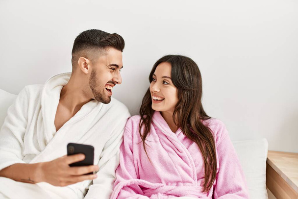 Young hispanic couple using smartphone lying on bed at home. - Photo, Image