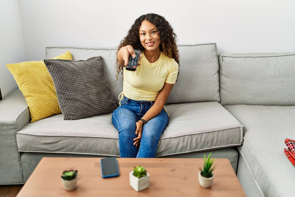 Mladý latina žena usměvavý jistý sledování televize doma - Fotografie, Obrázek