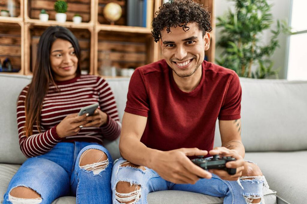 Man playing video game and woman using smartphone at home. - Photo, Image