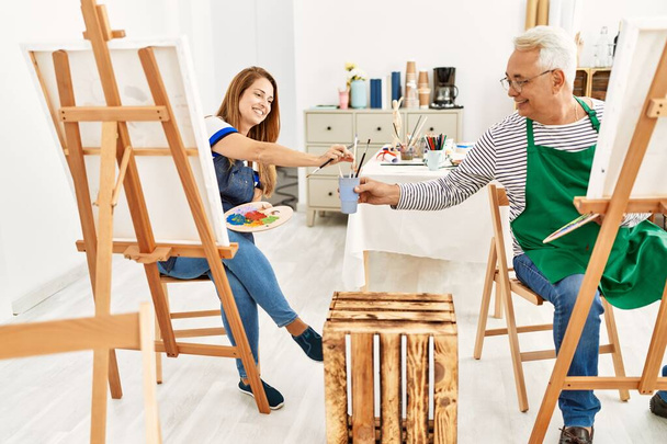 Deux artistes d'âge moyen souriant heureux peinture au studio d'art. - Photo, image
