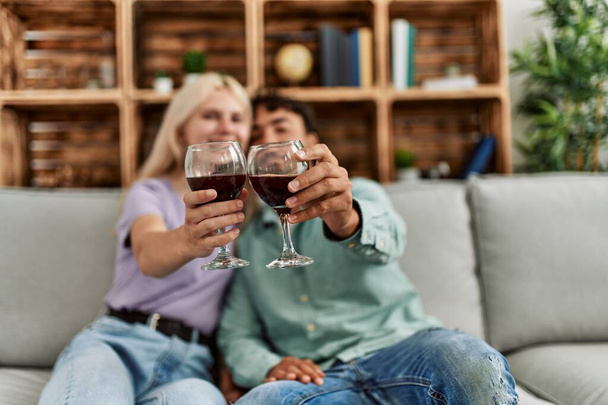 Junges Paar lächelt glücklich beim Anstoßen mit Rotweinglas zu Hause. - Foto, Bild