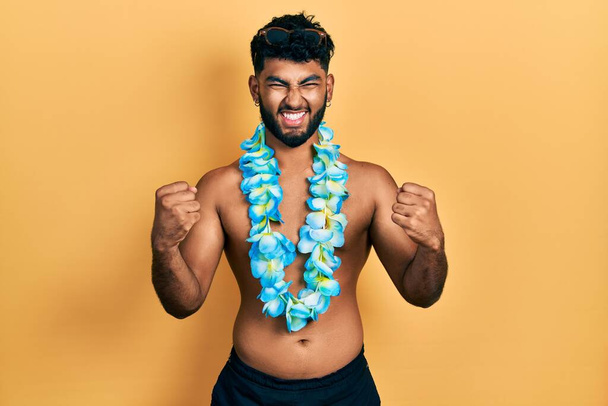 Араб с бородой в купальнике и гавайские леи гордо кричат, празднуя победу и успех, очень взволнованный поднятыми руками  - Фото, изображение