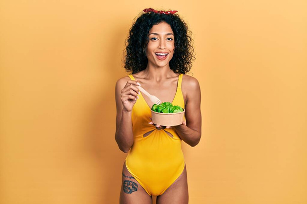 Young latin girl wearing swimsuit eating salad celebrating crazy and amazed for success with open eyes screaming excited.  - Fotoğraf, Görsel