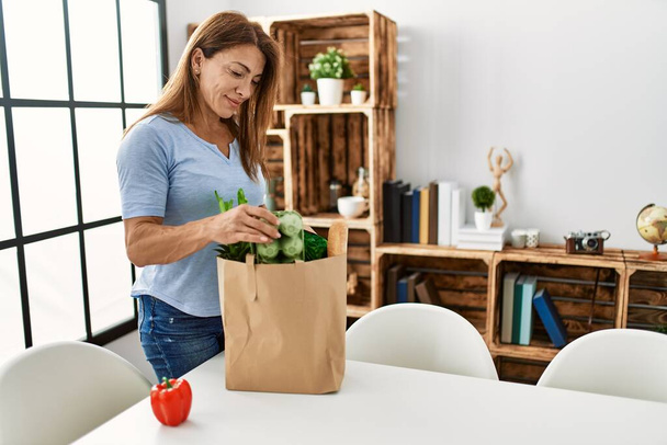 Middle age caucasian woman holding paper bag with groceries standing at home. - Photo, Image