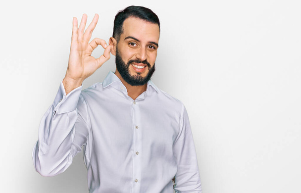 Young man with beard wearing business shirt smiling positive doing ok sign with hand and fingers. successful expression.  - Foto, Imagem