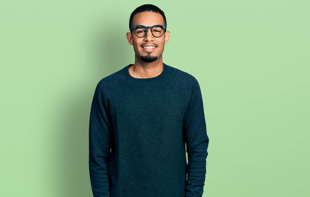 Junger afrikanisch-amerikanischer Mann in lässiger Kleidung und Brille mit einem fröhlichen und kühlen Lächeln im Gesicht. Glück gehabt.  - Foto, Bild