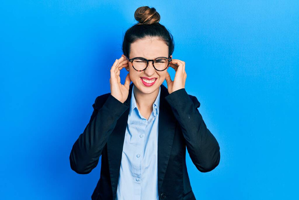 Young hispanic girl wearing business clothes and glasses covering ears with fingers with annoyed expression for the noise of loud music. deaf concept.  - Photo, Image