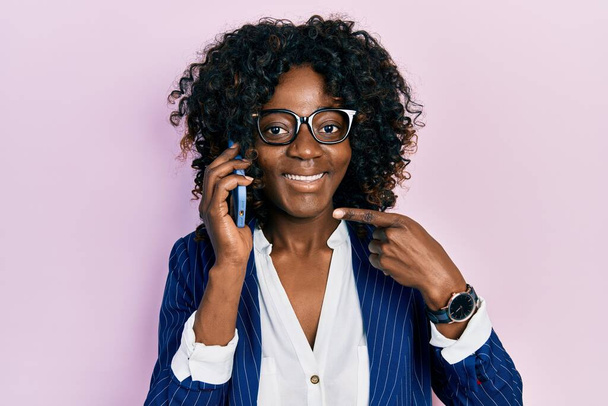 Genç Afro-Amerikalı kadın akıllı telefondan konuşuyor. Gülümsüyor, mutlu bir şekilde el ve parmak işareti yapıyor.  - Fotoğraf, Görsel
