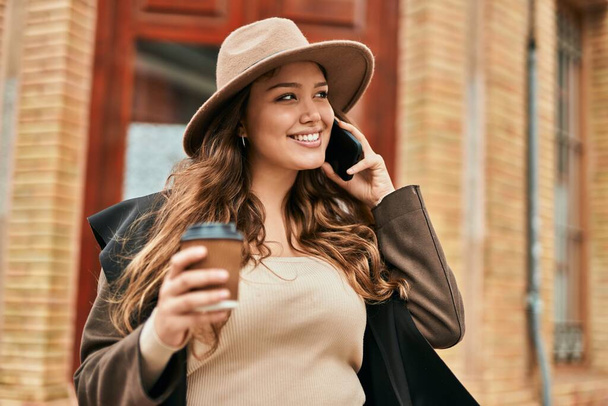 Молода іспаномовна туристична жінка розмовляє по смартфону і п'є каву в місті
. - Фото, зображення