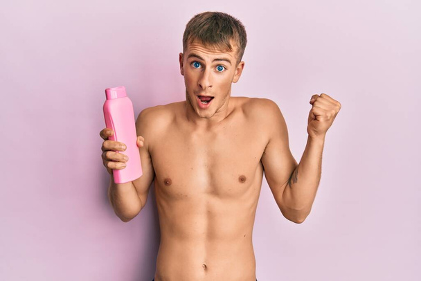 Genç beyaz adam elinde şampuan şişesi ile gururla bağırıyor zaferi ve başarıyı kutluyor.  - Fotoğraf, Görsel