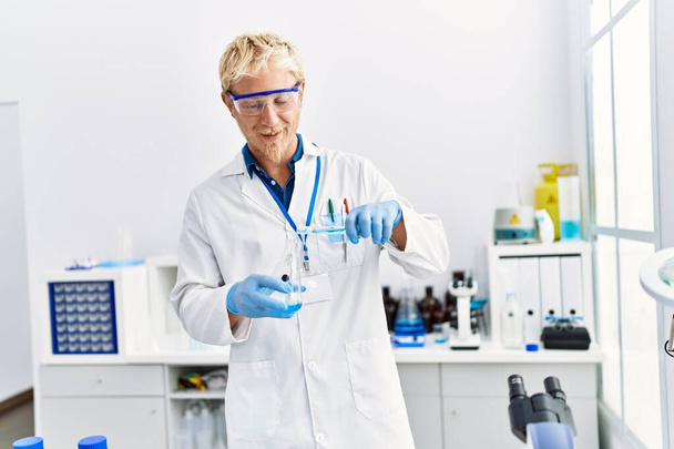 Jovem caucasiano vestindo cientista uniforme segurando tubo de ensaio em laboratório - Foto, Imagem
