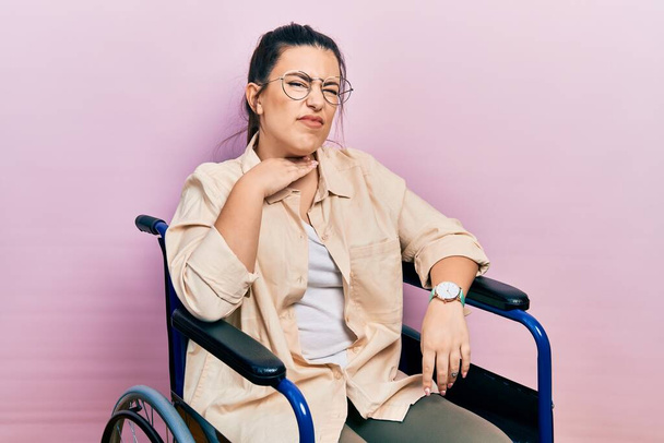 Junge hispanische Frau sitzt im Rollstuhl und schneidet sich mit der Hand als Messer die Kehle durch, droht Aggression mit wütender Gewalt  - Foto, Bild