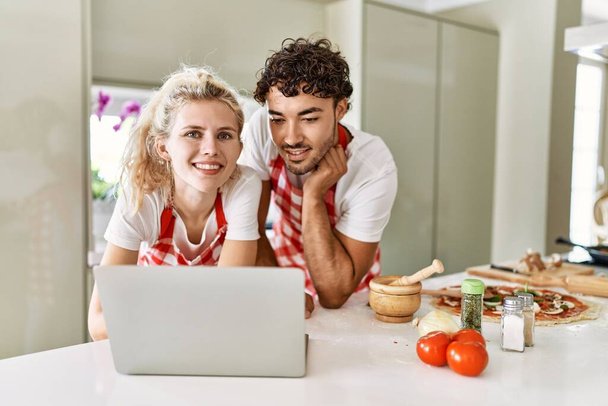 Young couple smiling happy using laptop at kitchen. - Valokuva, kuva
