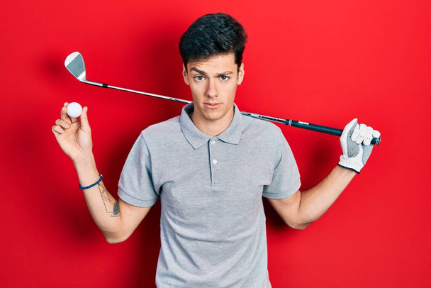 Young hispanic man holding golf ball skeptic and nervous, frowning upset because of problem. negative person.  - Fotoğraf, Görsel