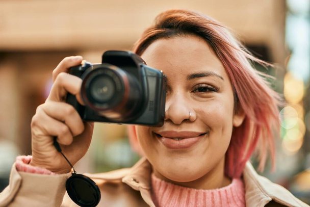 Giovane ragazza ispanica sorridente felice con fotocamera reflex in città. - Foto, immagini