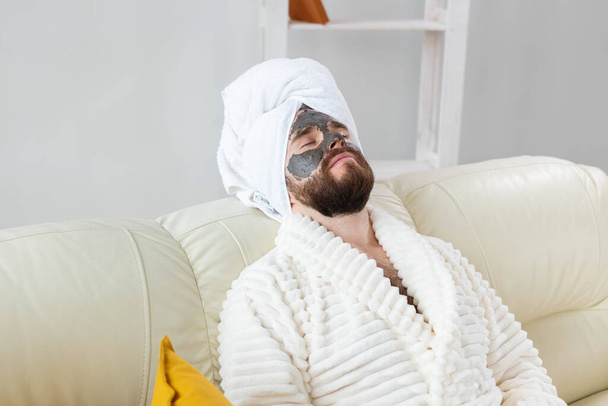 Bearded man has clean fresh skin, wears beauty clay mask on face and enjoys beauty treatments. Spa at home, body and skin care - Fotoğraf, Görsel
