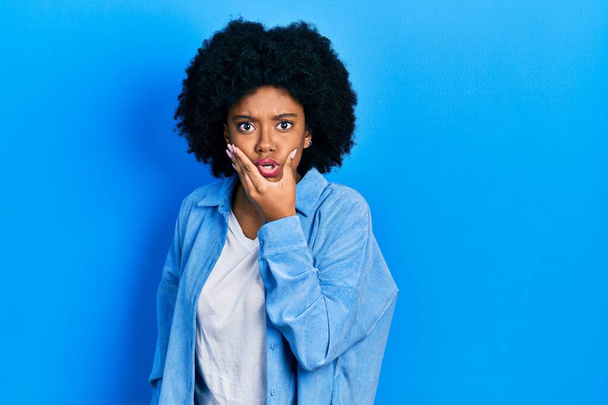 jonge afrikaanse amerikaanse vrouw dragen casual kleding op zoek gefascineerd door ongeloof, verrassing en verbaasd uitdrukking met handen op kin  - Foto, afbeelding
