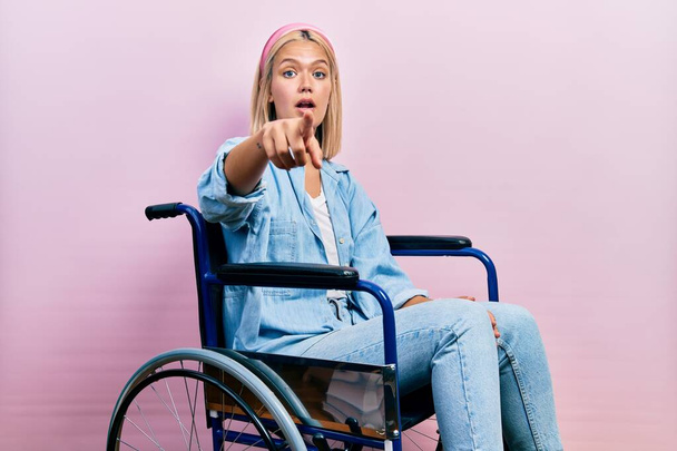 Kaunis blondi nainen istuu pyörätuolilla osoittaen tyytymätön ja turhautunut kameraan, vihainen ja raivoissaan sinulle  - Valokuva, kuva