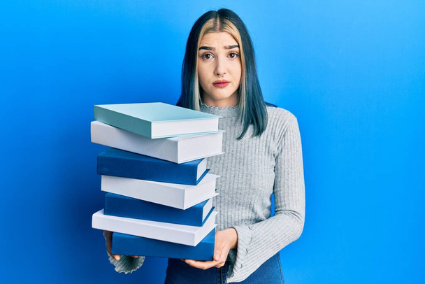 Joven chica moderna sosteniendo una pila de libros escéptico y nervioso, frunciendo el ceño molesto debido a un problema. persona negativa.  - Foto, Imagen