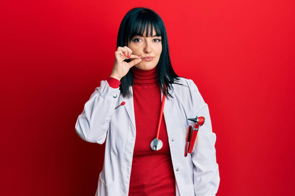 Young hispanic woman wearing doctor uniform and stethoscope mouth and lips shut as zip with fingers. secret and silent, taboo talking  - Fotografie, Obrázek