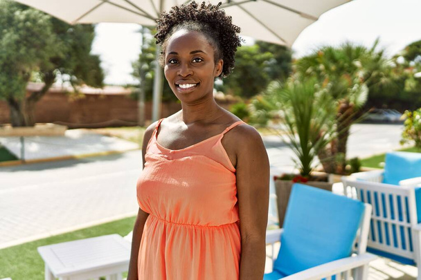 Νεαρή Αφροαμερικανή που χαμογελάει ευτυχισμένη μια καλοκαιρινή μέρα δίπλα στο μπαρ. - Φωτογραφία, εικόνα