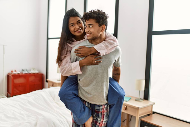 Young latin couple smiling happy standing at the bedroom. Man holding woman on his back. - Fotoğraf, Görsel