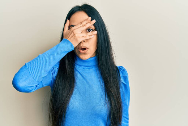 Young hispanic girl wearing casual clothes peeking in shock covering face and eyes with hand, looking through fingers afraid  - Photo, Image
