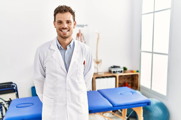 Knappe jongeman die werkt in een pijnkliniek met een blije en coole glimlach op zijn gezicht. gelukkig persoon.  - Foto, afbeelding