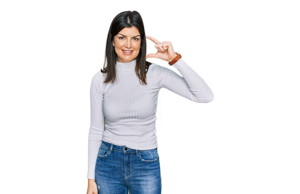 Beautiful brunette woman wearing casual clothes smiling and confident gesturing with hand doing small size sign with fingers looking and the camera. measure concept.  - Photo, Image