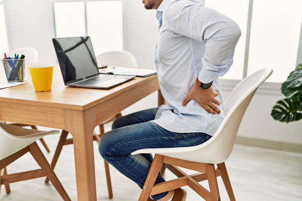 Молодой латиноамериканец работает в офисе. Сидя на столе с болью в спине. - Фото, изображение