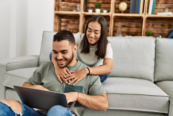Joven pareja latina sonriendo feliz usando portátil en casa. - Foto, imagen