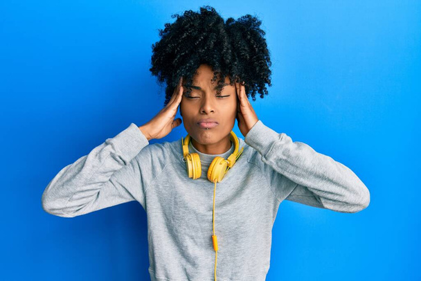Африканська американка з волоссям афроамериканки в светрі і навушниками, які страждають від головного болю і стресу, тому що біль і мігрень. руки на голові.  - Фото, зображення