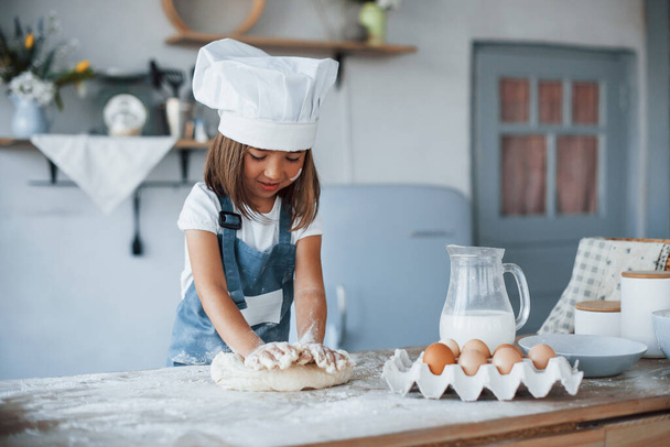 Cute kid in white chef uniform preparing food on the kitchen. - Photo, Image