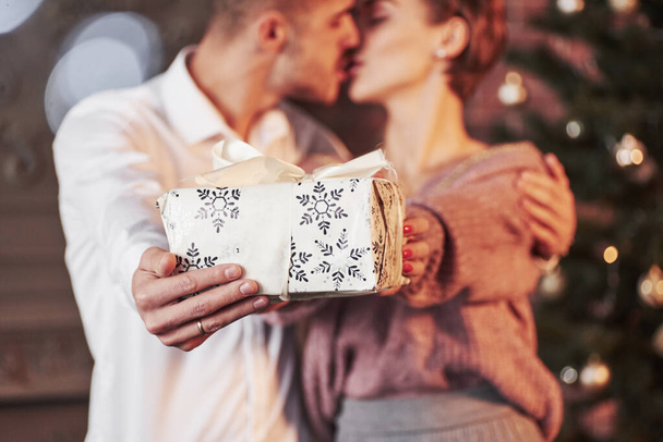 Kissing while holding gift box. Cute people. Nice couple celebrating new year in the new year decorated room. - Foto, Imagem