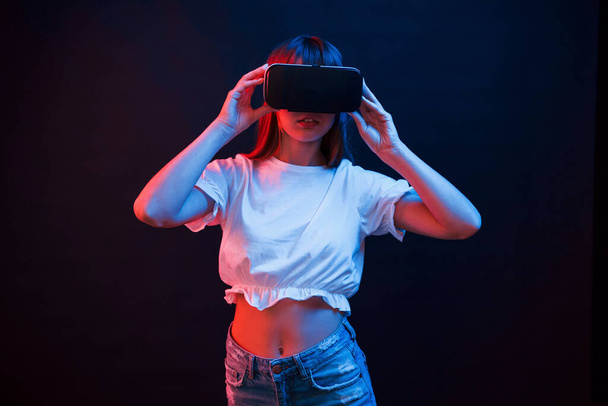 Impressed girl. Young woman using virtual reality glasses in the dark room with neon lighting. - Fotografie, Obrázek