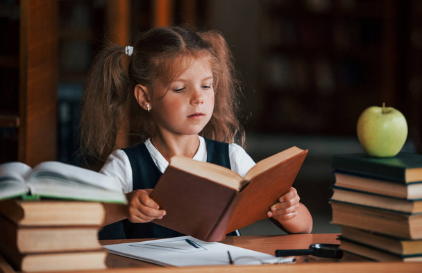 Cute little girl with pigtails is in the library. Apple on the books. - Φωτογραφία, εικόνα