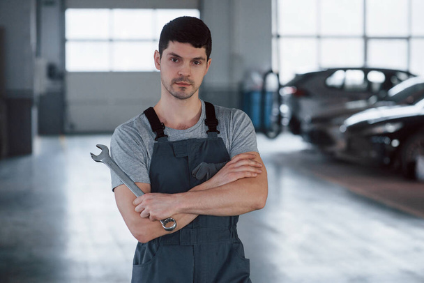 All for your vehicle. Portrait of serious worker in uniform that stands in his workshop with wrench in hand. - Φωτογραφία, εικόνα