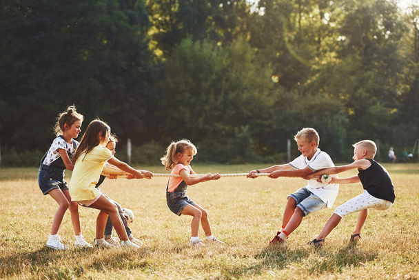 Kids playing tug of war game in the beautiful meadow at sunny day. - Photo, image