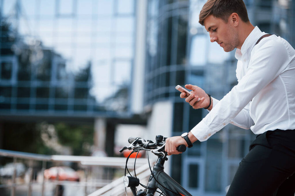 Blurred background. Businessman in formal clothes with black bicycle is in the city. - Foto, Imagen